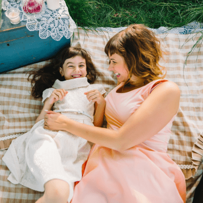 Mom and daughter hugging on a blanket on the grass in the Park